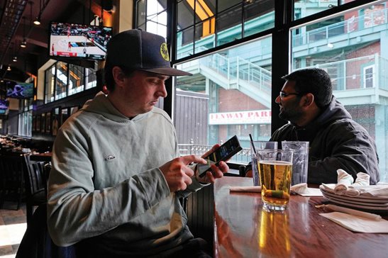 Taylor Foehl, left, of Boston, looks at a mobile betting app on his phone Friday at the Cask ‘N Flagon near Fenway Park. People in Massachusetts, Ohio and Kansas will be able to cast online bets on the NCAA basketball tournament, which starts Thursday, for the first time this year. A total of 33 states including Illinois now allow at least some form of sports wagering. States have moved rapidly to enter the market since a U.S. Supreme Court ruling allowed it almost five years ago.